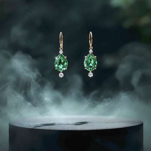 Green teardrop earrings with gold accents on a dark pedestal with smoke effect